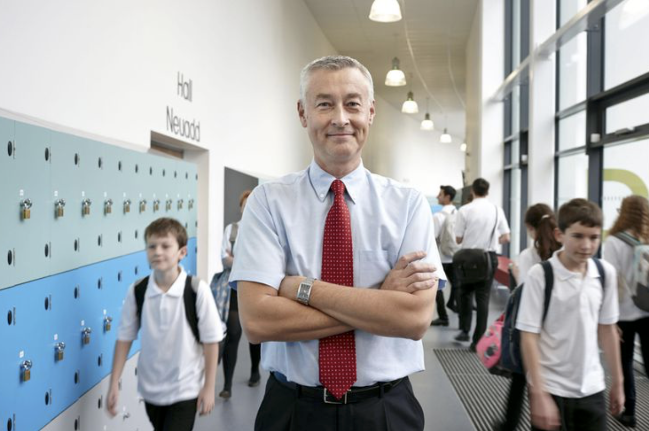Adult male in poses in hallway with grade school students walking in background